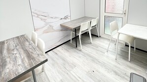 A modern room with a wooden ceiling, white walls, and a marble accent wall. There is a wooden table with two white chairs, a window, and a trash bin. - Addison's Adorable Abode (Pembroke Dock)
