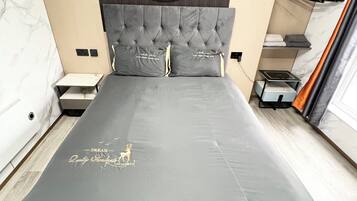 Ein modernes Schlafzimmer mit einer gesteppten Kopfteil, einer großen runden Wanddekoration und einem Bett mit grauem Matratze und dekorativem Text.