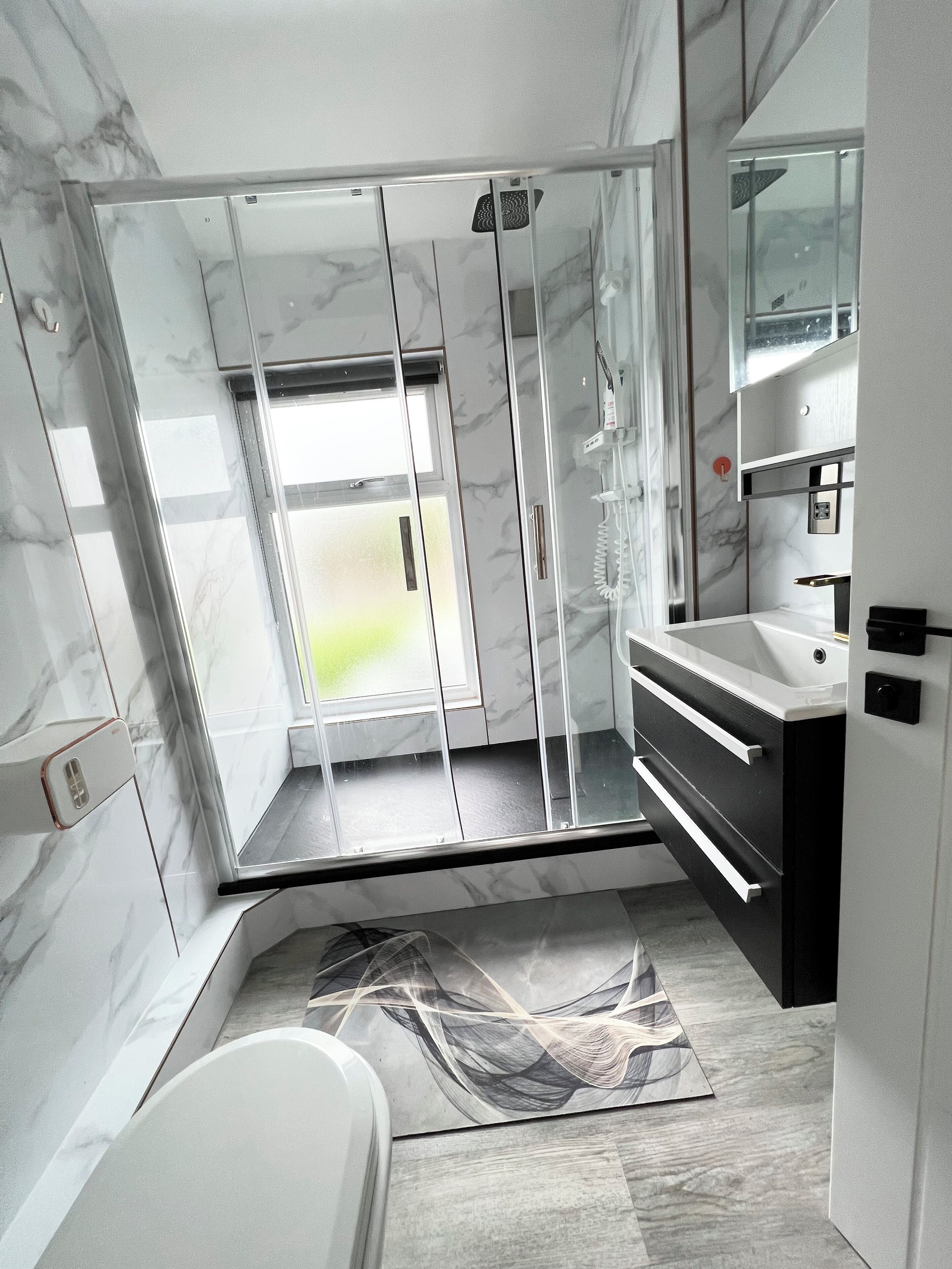 Un baño moderno con ducha envuelta en vidrio, un lavamanos blanco y piso de baldosas de mármol.
