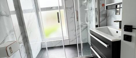 A modern bathroom with a glass-enclosed shower, a white sink, and a marble-tiled floor.