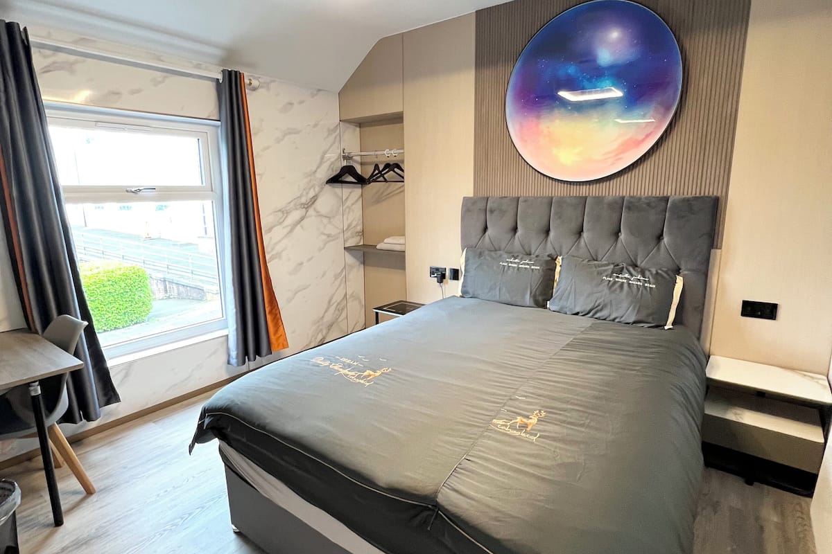 Une chambre moderne avec un grand lit, un élément de décoration circulaire au mur, une armoire intégrée et une vue par la fenêtre.
