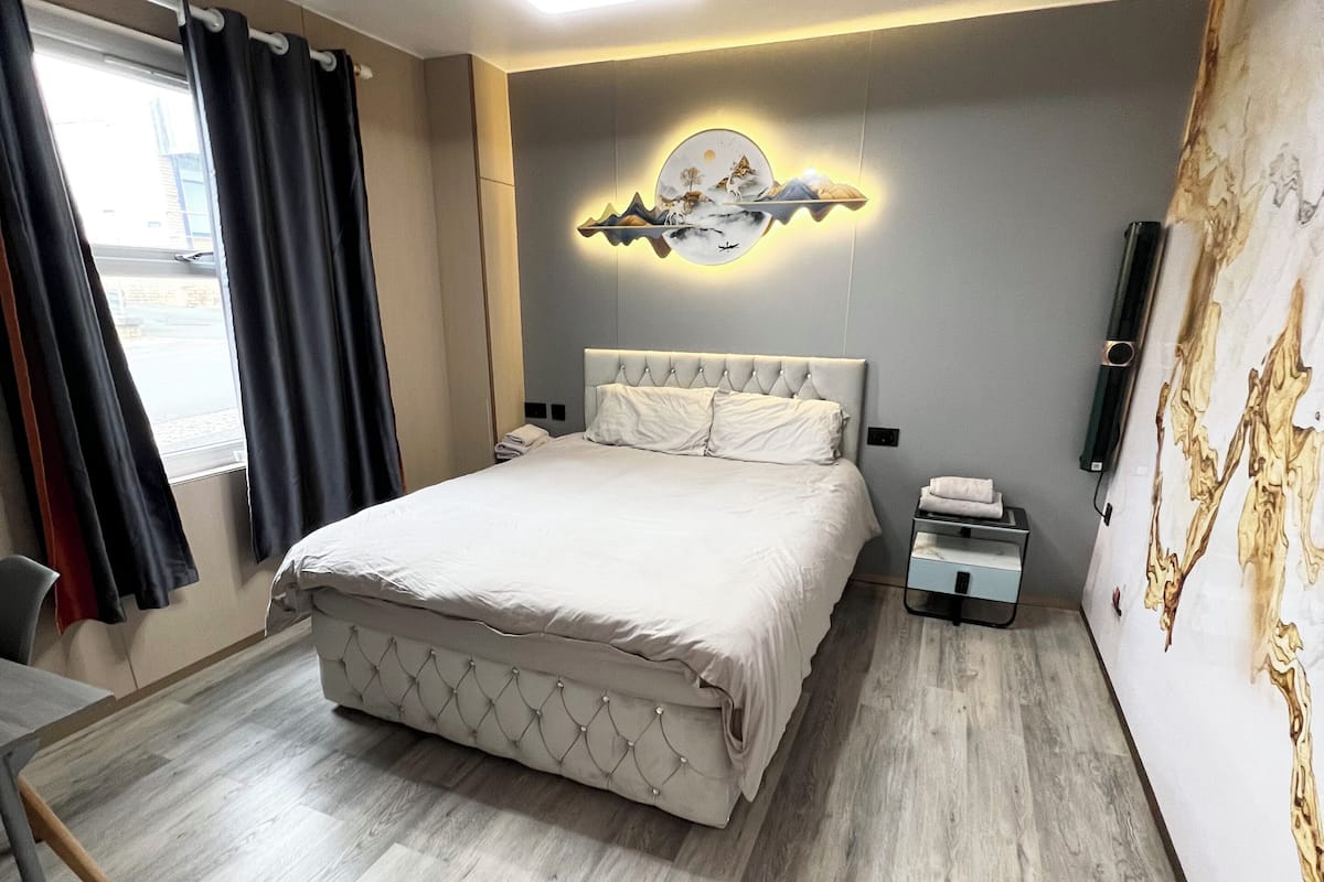 Une chambre d’hôtel moderne, dotée d’un grand lit, d’une table de chevet, d’un téléviseur fixé au mur et d’une fenêtre avec des rideaux.