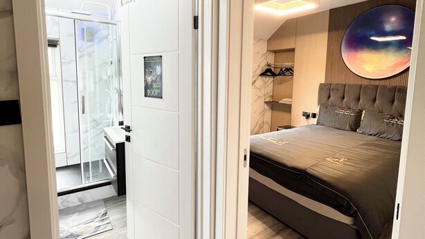 A bedroom with a bed, a nightstand, a wall-mounted circular artwork, and a bathroom visible through an open door. - Addison's Adorable Abode (Pembroke Dock)