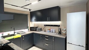A modern kitchen with dark cabinets, a stainless steel refrigerator, and a wooden countertop. - Addison's Adorable Abode (Pembroke Dock)