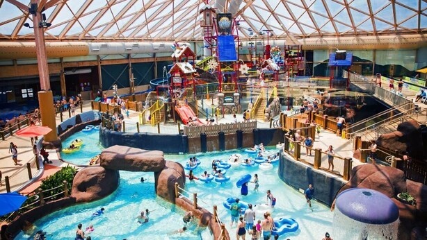 Un parque acuático interior con múltiples toboganes de agua, piscinas y zonas de juegos.