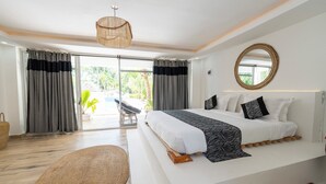 Un dormitorio moderno con una cama grande, un espejo redondo y vistas a un patio con mobiliario exterior.
