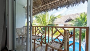 Un balcón con mobiliario de mimbre, una piscina y palmeras.