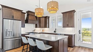 Een moderne keuken met donkerhouten kastjes, roestvrijstalen apparatuur, een groot eiland met barkrukken en uitzicht door een geopende deur.