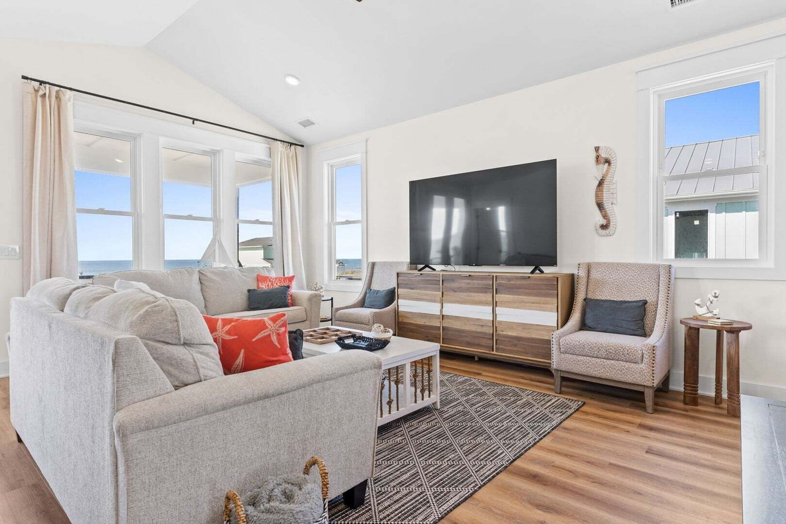 A living room with a sofa, armchair, TV, and a view of the sea.
