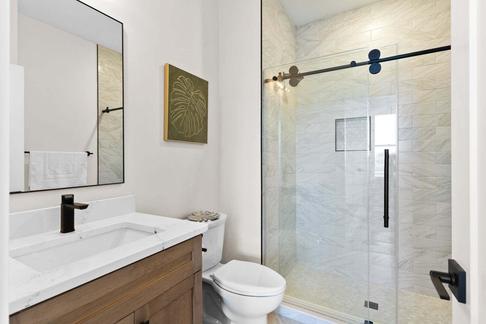 Un bagno moderno con box doccia in vetro, un water bianco e un mobile lavabo con specchio e porta asciugamani.
