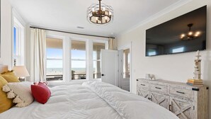 Een slaapkamer met een groot bed, een televisie, een decor kast en uitzicht op zee.