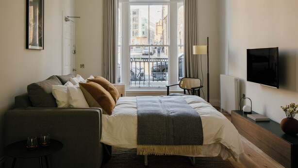 A modern hotel room with a large bed, a sofa, a small table, a chair, a TV, and a window with a view of the city. - 33 Castle Terrace (Edinburgh)