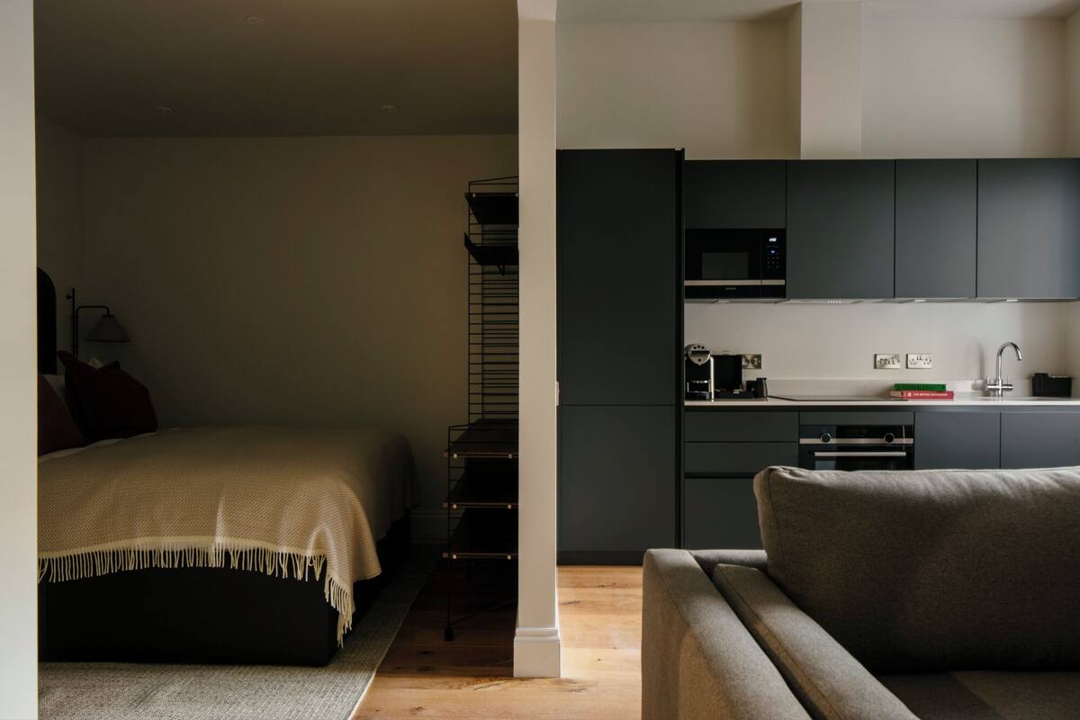 A modern hotel room with a bed, a sofa, a kitchenette, and a staircase.