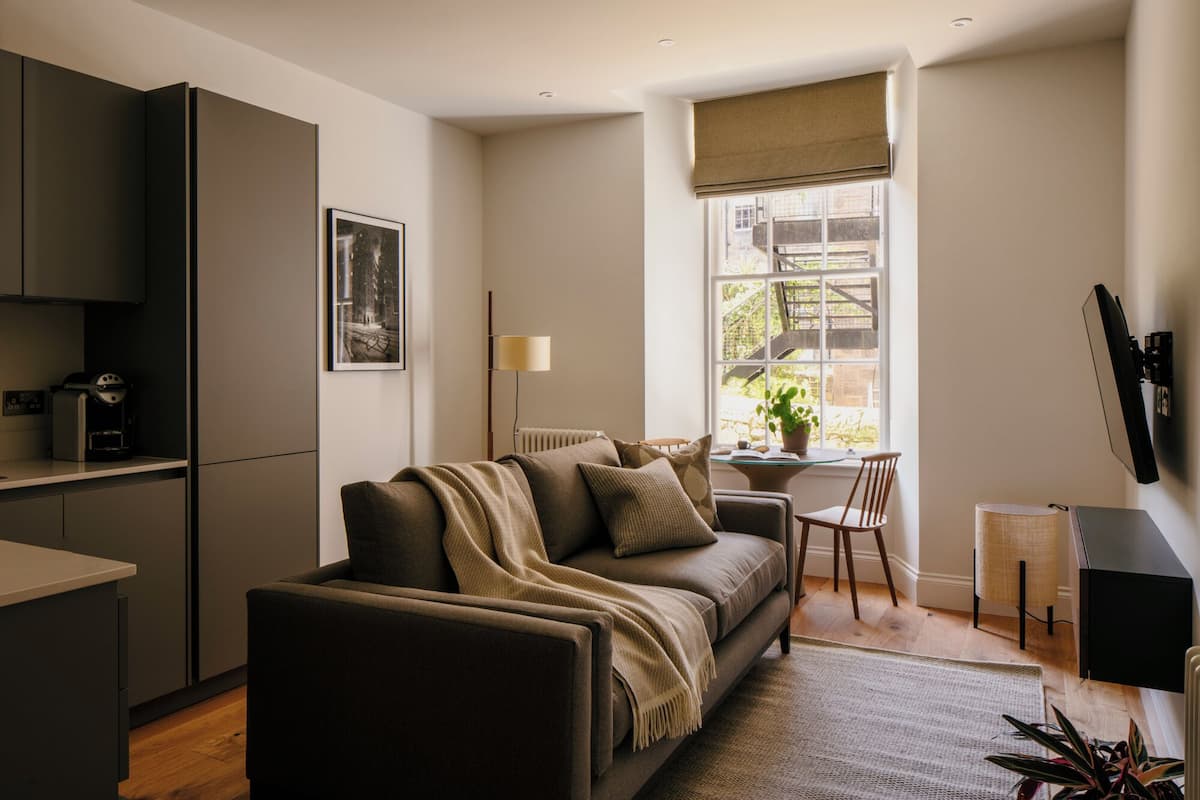 A modern living room with a sofa, a coffee machine, and a window with a view of a staircase.