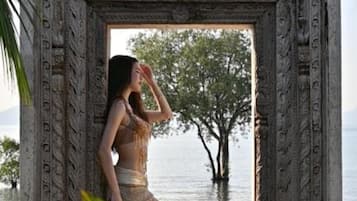 A person standing in an ornate doorway with intricate carvings, overlooking a body of water and trees.