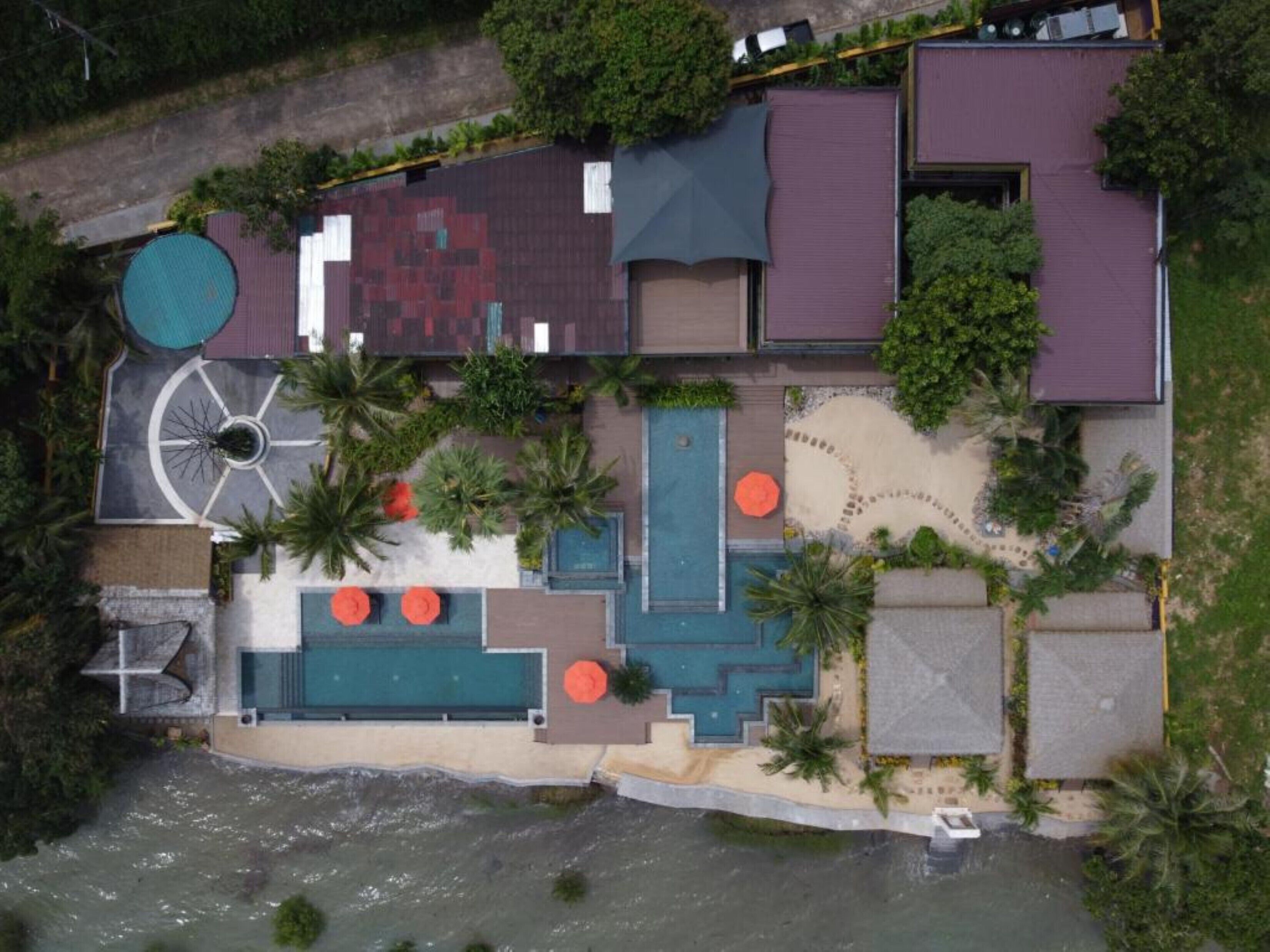 Vue aérienne d’un complexe hôtelier doté d’une piscine, d’un espace de détente en plein air et d’une plage.