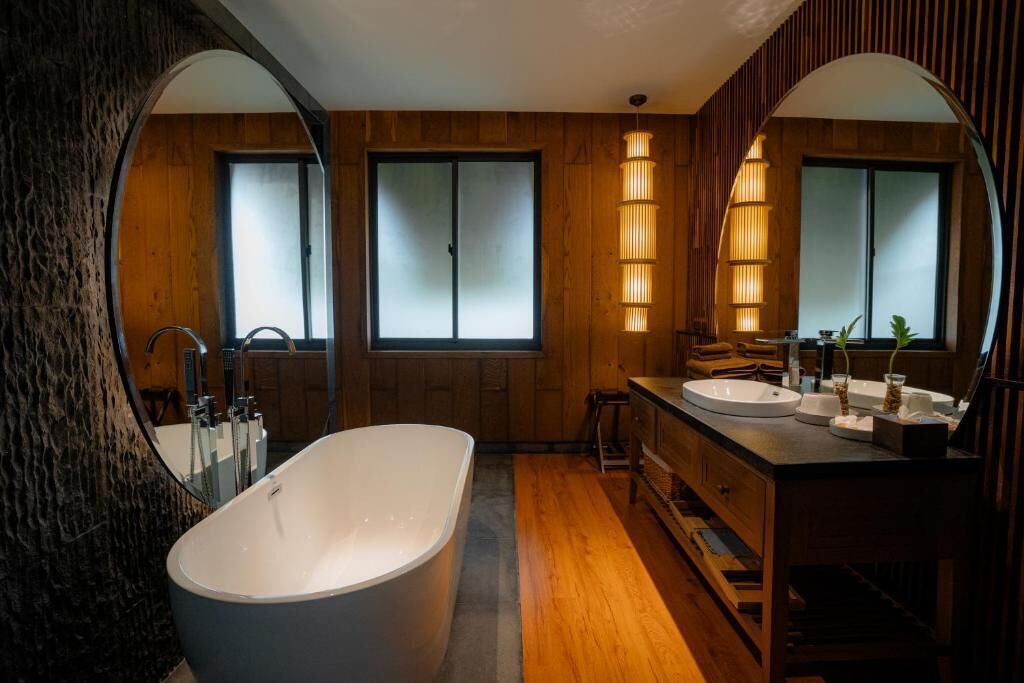 A modern bathroom with a freestanding bathtub, wooden vanity, and mirrored cabinets.