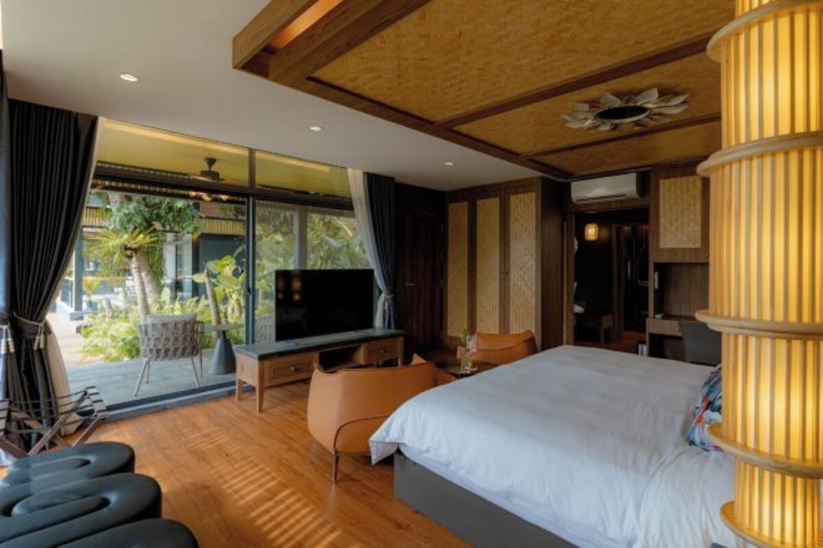 Habitación de hotel moderna con una cama grande, televisión, escritorio y balcón con vistas a zonas verdes.