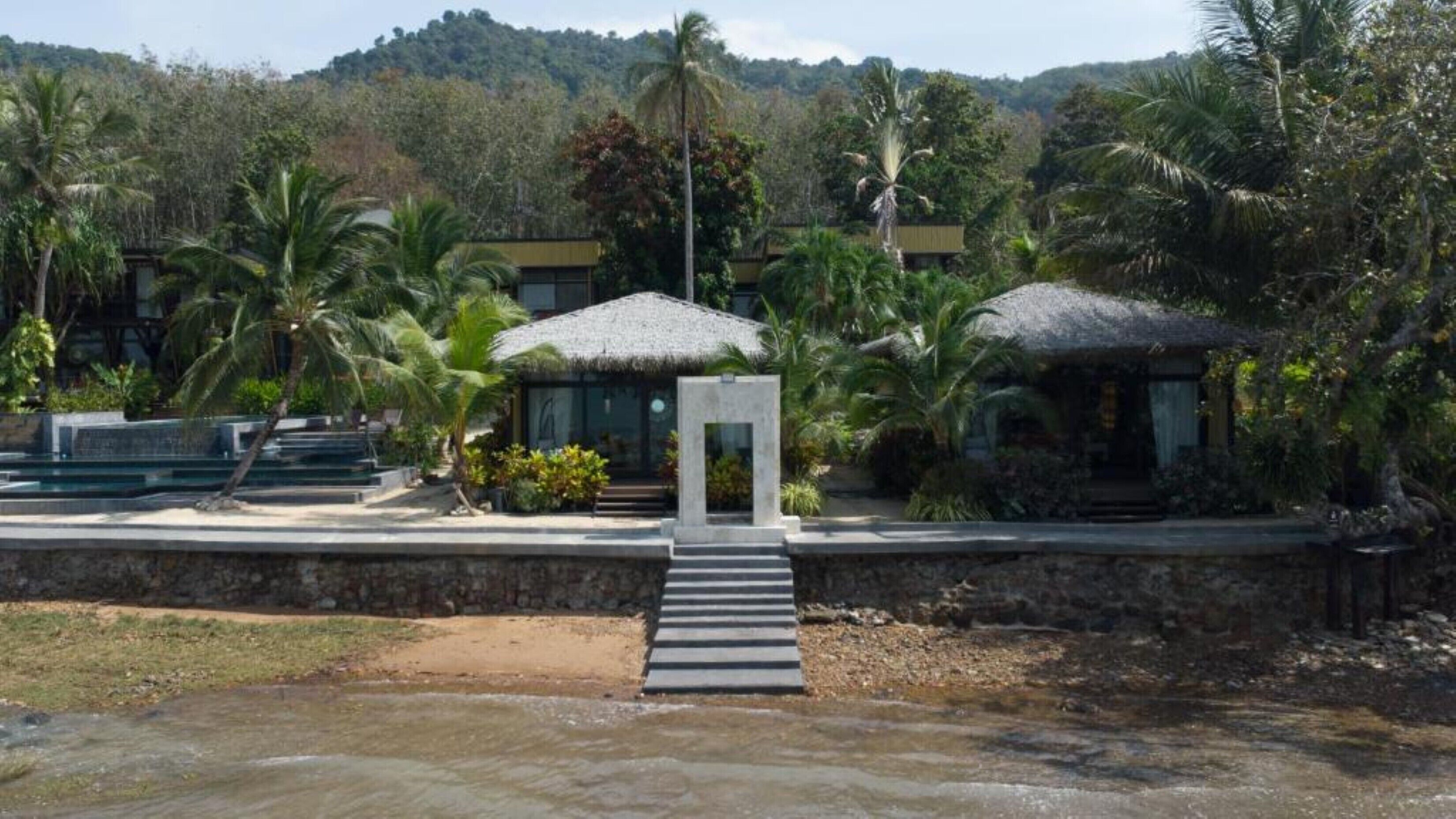Un resort con muro de piedra, piscina y estructuras de techo de paja.