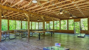 A covered picnic area with wooden benches and tables, large windows, and a wooden floor.