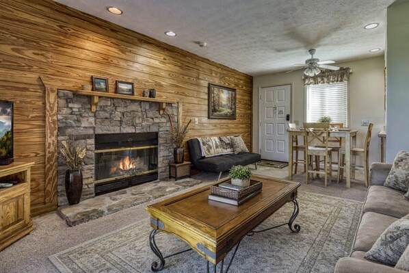 A living room with a stone fireplace, a sofa, a coffee table, and a dining area with a table and chairs.