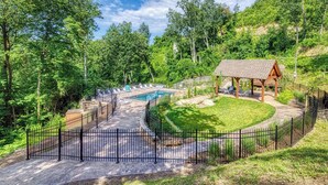 A pool area with a wooden deck, lounge chairs, and a gazebo.