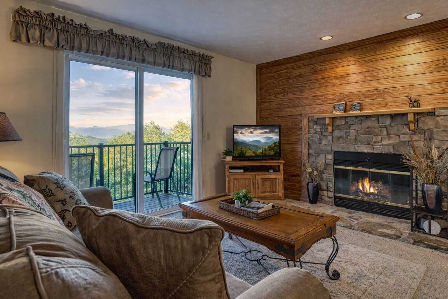 A living room with a sofa, a coffee table, a television, a fireplace, and a balcony with a chair.