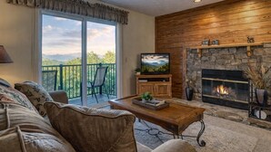 A living room with a sofa, a coffee table, a television, a fireplace, and a balcony with a chair.