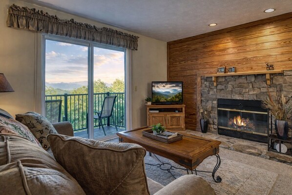 Una sala de estar con sofá, mesa de centro, televisión, chimenea y un balcón con una silla.