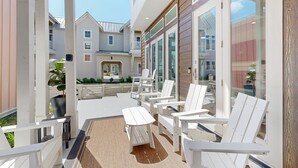 A covered outdoor seating area with white chairs and a table, overlooking a residential neighborhood. - Resort Pools, Golf Cart Boardwalk to the Beach (Port Aransas)