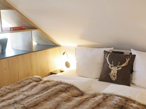 Een slaapkamer met een bed, nachtkastje, lamp en een houten plank met boeken.