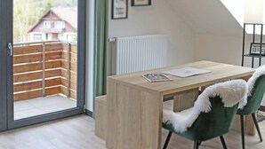 Moderni huone, jossa on puinen työpöytä, vihreä tuoli, jossa on pehmeä heittopeitto, patteri ja lasiovesta avautuva näkymä taloon.