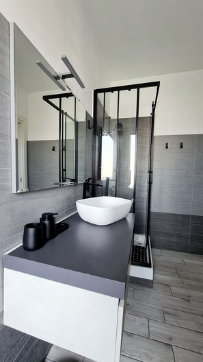 A modern bathroom with a large white sink, a glass shower enclosure, and a large mirror. - Severis Apartment Fiumicino  (Isola Sacra)