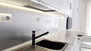 Une cuisine moderne au design épuré, dotée d’un évier en acier inoxydable, d’un robinet noir et d’un four encastré.
