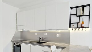Une cuisine moderne avec des meubles blancs, un four encastré, une cuisinière en acier inoxydable et un coin repas comprenant une table et des chaises.