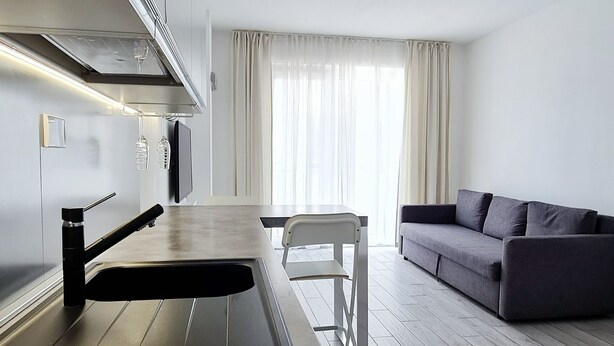 Une cuisine moderne dotée d’une cuisinière intégrée, d’une petite table à manger et d’un canapé dans l’espace salon.