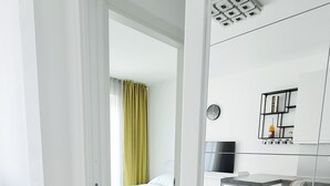Une chambre d’hôtel moderne avec un plancher en bois, un lit avec une literie verte, un bureau avec une chaise et un téléviseur fixé au mur.
