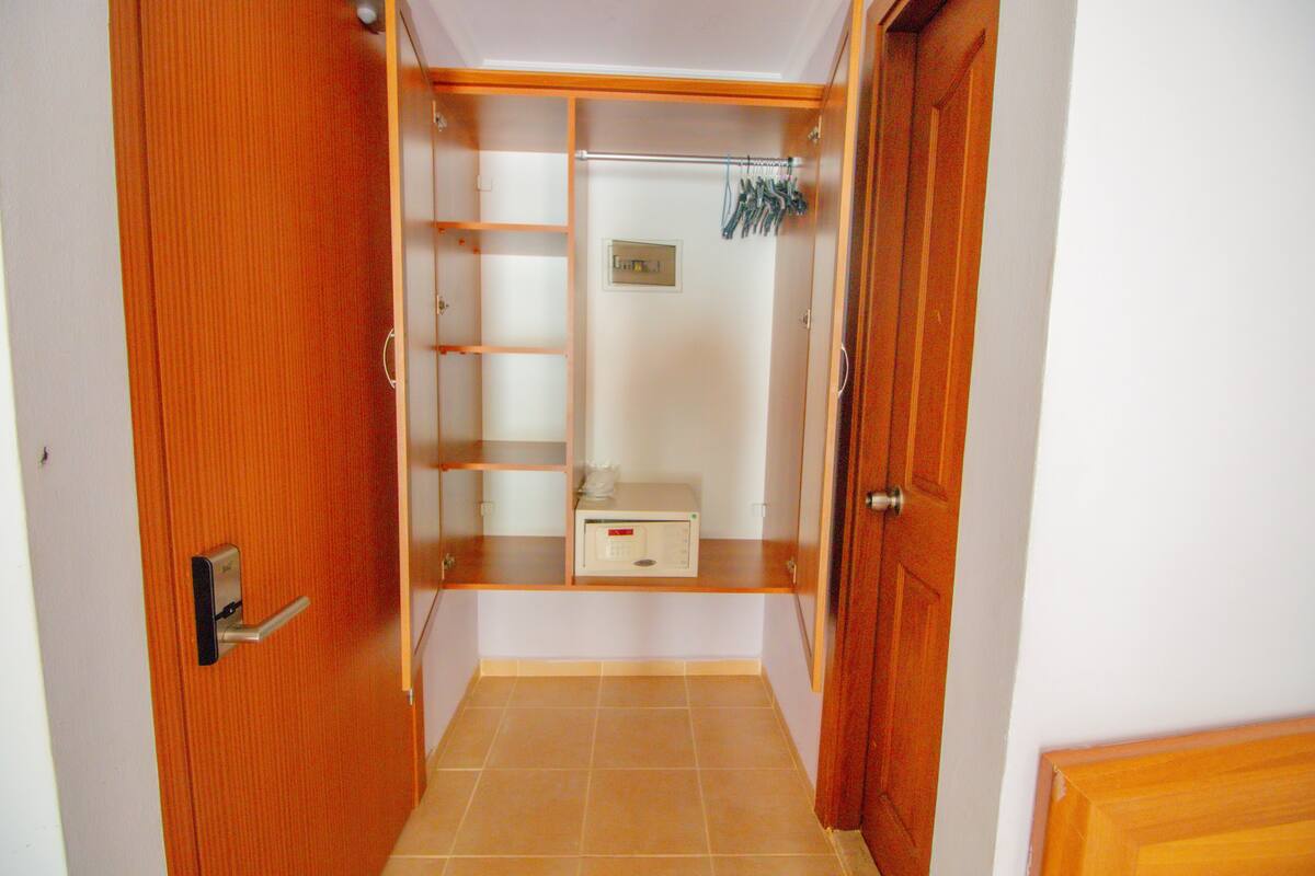 Un couloir avec une porte en bois sur la gauche, un sol carrelé et une armoire en bois dotée d’étagères et d’une tringle pour suspendre les vêtements.