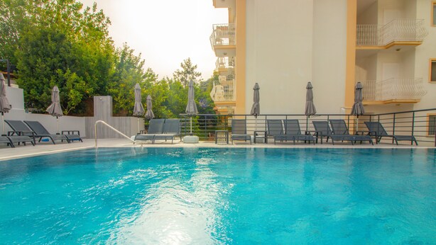 A swimming pool with lounge chairs and umbrellas, surrounded by a building with balconies. - Celeste Hotel (Fethiye)