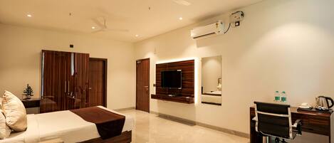 A hotel room with a bed, a desk, a chair, a television, and an air conditioning unit.