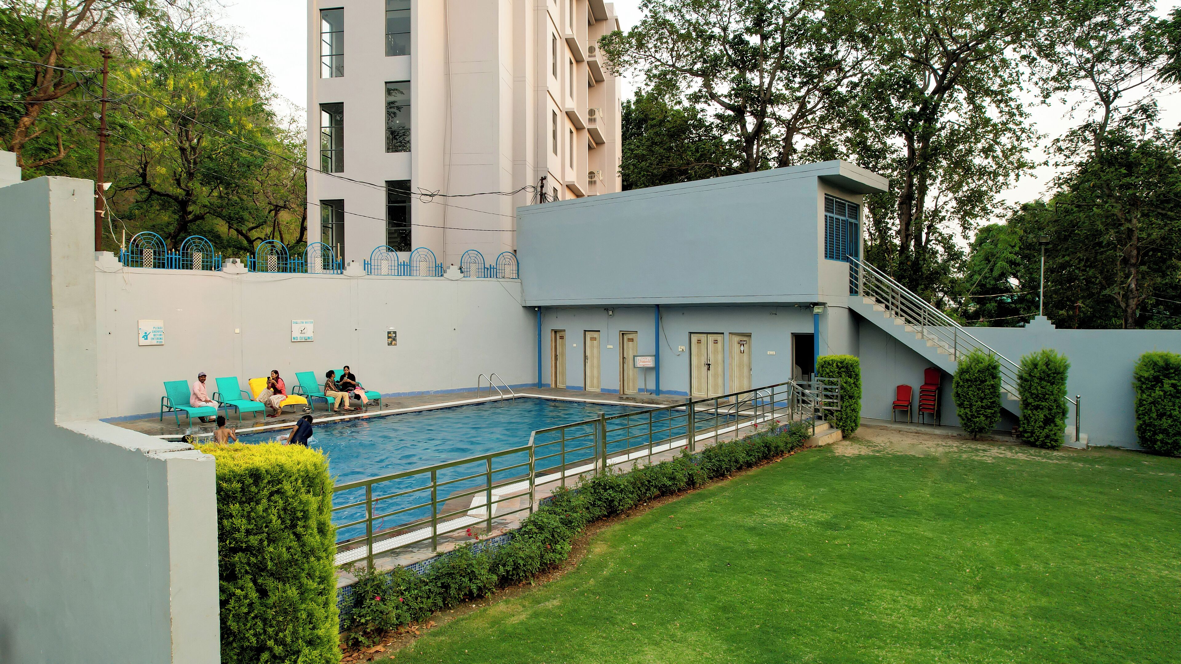 A swimming pool area with a modern building, a grassy lawn, and a staircase leading to a second floor.