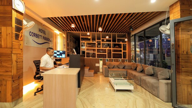 A hotel reception area with a wooden reception desk, a sofa, and a glass coffee table. - Hotel Corbett Paradise Kotdwar (Lansdowne)