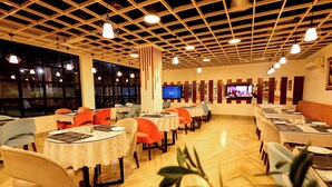 A restaurant with multiple tables and chairs, a television screen, and a wooden ceiling. - Hotel Corbett Paradise Kotdwar (Lansdowne)