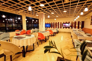 A restaurant with multiple tables and chairs, a television screen, and a wooden ceiling.