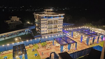 A multi-story hotel with a rooftop terrace, outdoor seating, and a stage for events.