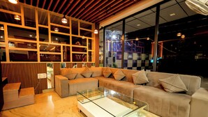 A modern living room with a sectional sofa, a glass coffee table, and a wooden accent wall with shelves. - Hotel Corbett Paradise Kotdwar (Lansdowne)