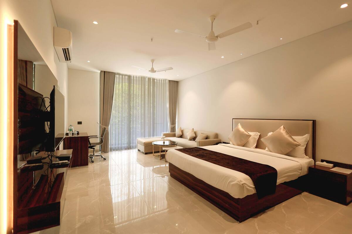 A modern hotel room with a large bed, a desk, a chair, and a TV.