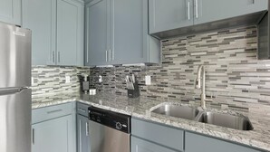 Cozinha moderna com armários cinza, geladeira de aço inoxidável, lava-louças e painel de azulejos.