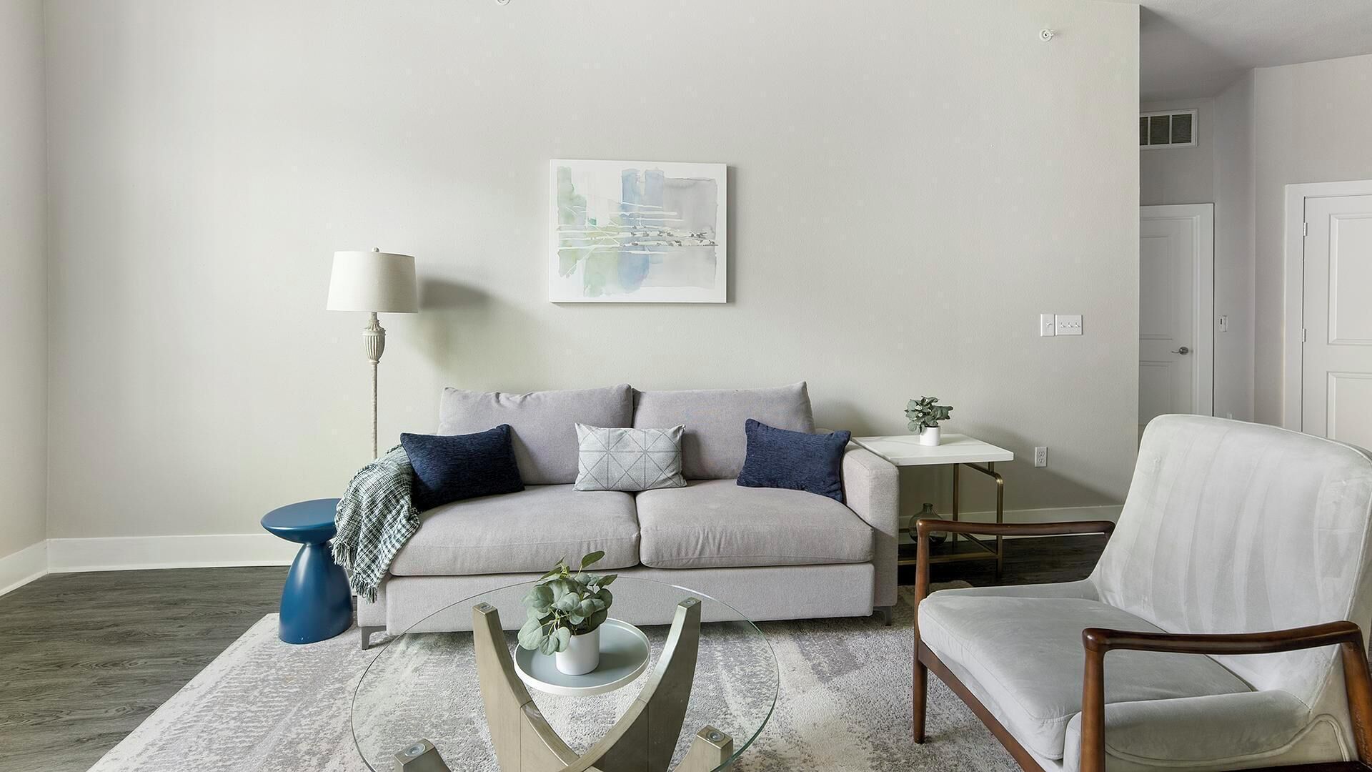 Un salón con un sofá gris, una mesita auxiliar azul, un sillón blanco y una lámpara de pie.