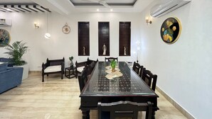Comedor con mesa de vidrio, sillas de madera oscura, lámpara de araña y aire acondicionado instalado en la pared.